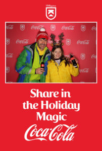 Photo booth picture of a father and daughter posing with Coca-Cola in the Coca-Cola Killington branded backdrop photo booth with a Share in the Holiday Magic frame