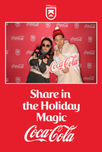A couple posing with Coca-Cola on a Coca-Cola Killington branded backdrop photo booth with a Share in the Holiday Magic frame