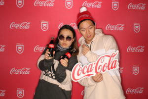 A couple posing with Coca-Cola on a Coca-Cola Killington branded backdrop photo booth