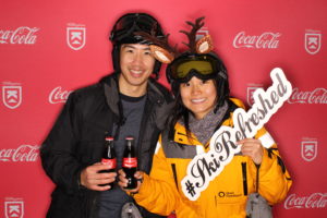 Two skiers posing with Coca-Cola on a Coca-Cola Killington branded backdrop photo booth