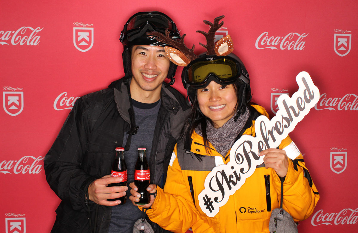 Two skiiers posing with Coca-Cola on a Coca-Cola Killington branded backdrop photo booth
