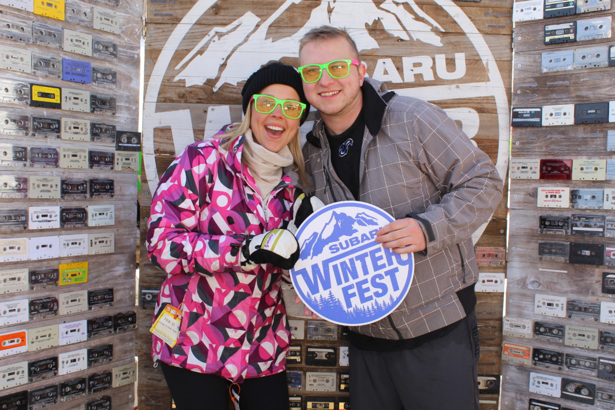 Couple holding a Subaru Winter Fest sign posing in the Subaru branded backdrop photo booth