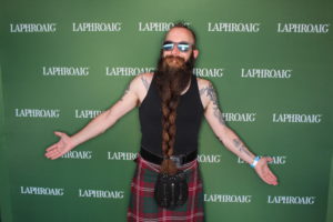 A man wearing a kilt posing with his arms open in a Laphroaig Whiskey branded backdrop photo booth