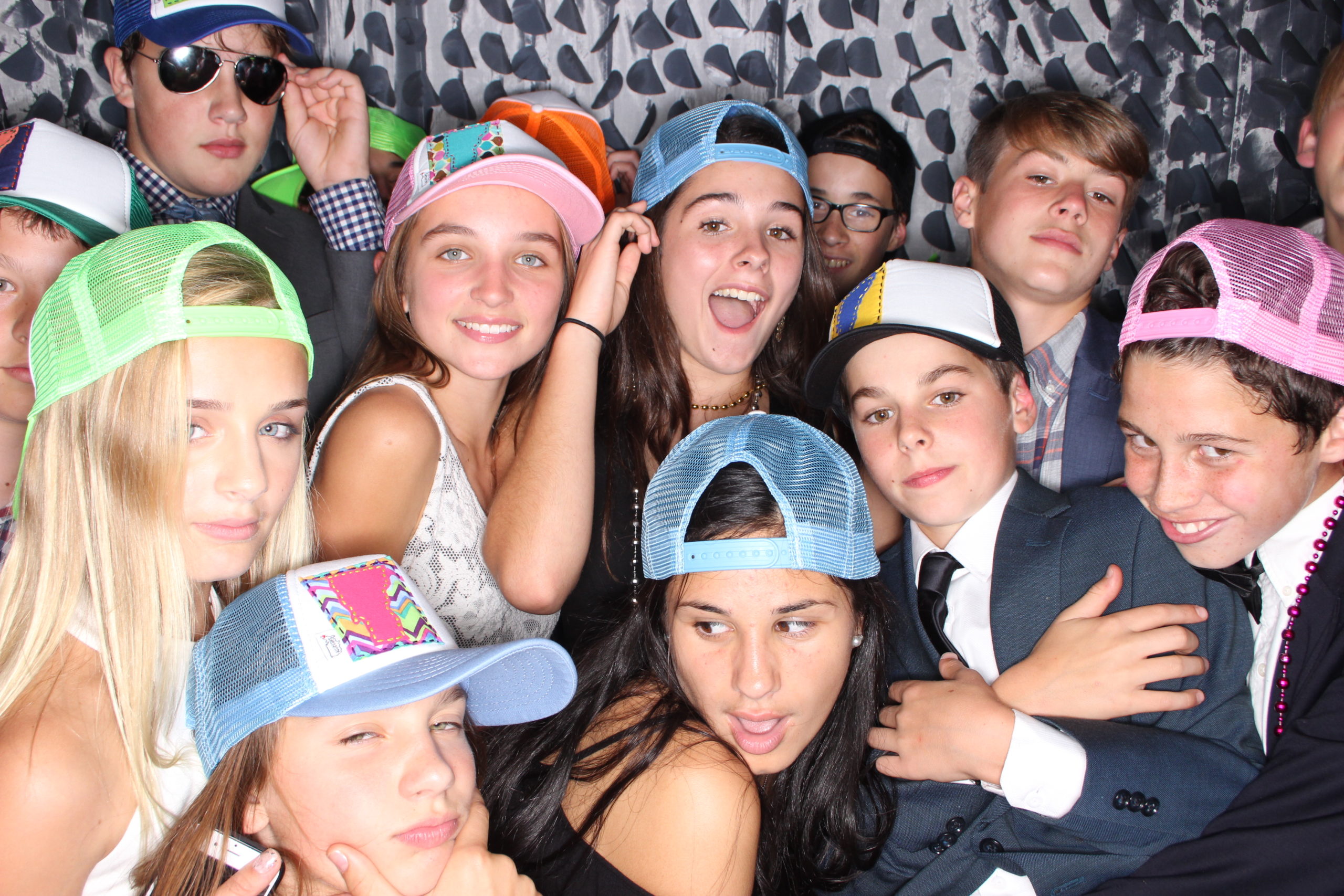 Group photo of teenagers posing with snap back hats in a photo booth
