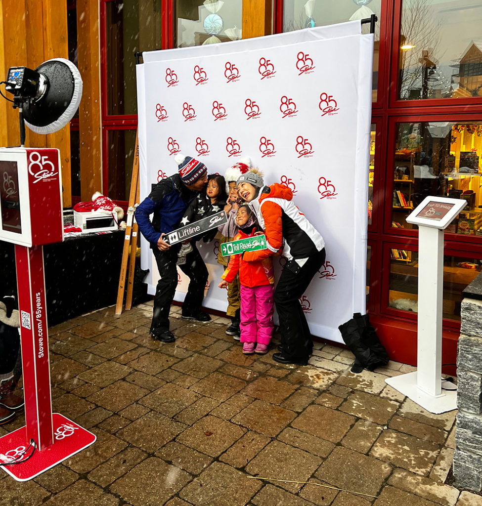 A family five hold ski signs and make goofy faces in front of a photo booth set up at Stowe Mountain Resort in VT