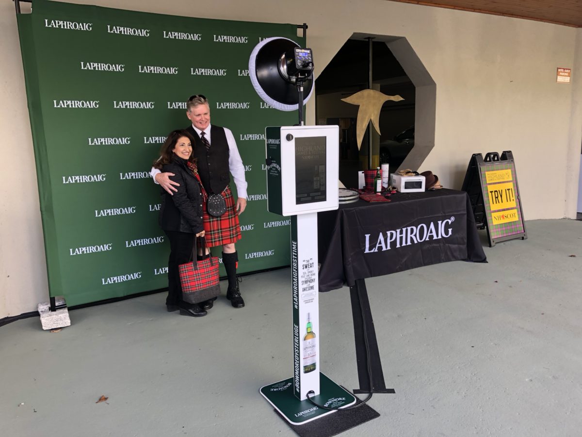 Overview of a couple posing for a picture in the Laphroaig Whiskey branded backdrop photo booth