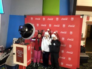 Overview shot of 3 women standing in a photo booth in front of a Coca-Cola Killington branded backdrop