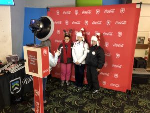 Woman explaining how to use the photo booth to 3 women standing in front of a Coca-Cola Killington branded backdrop