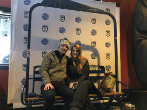 Couple sitting on a ski lift in front of a Subaru Winter Fest at Killington branded backdrop