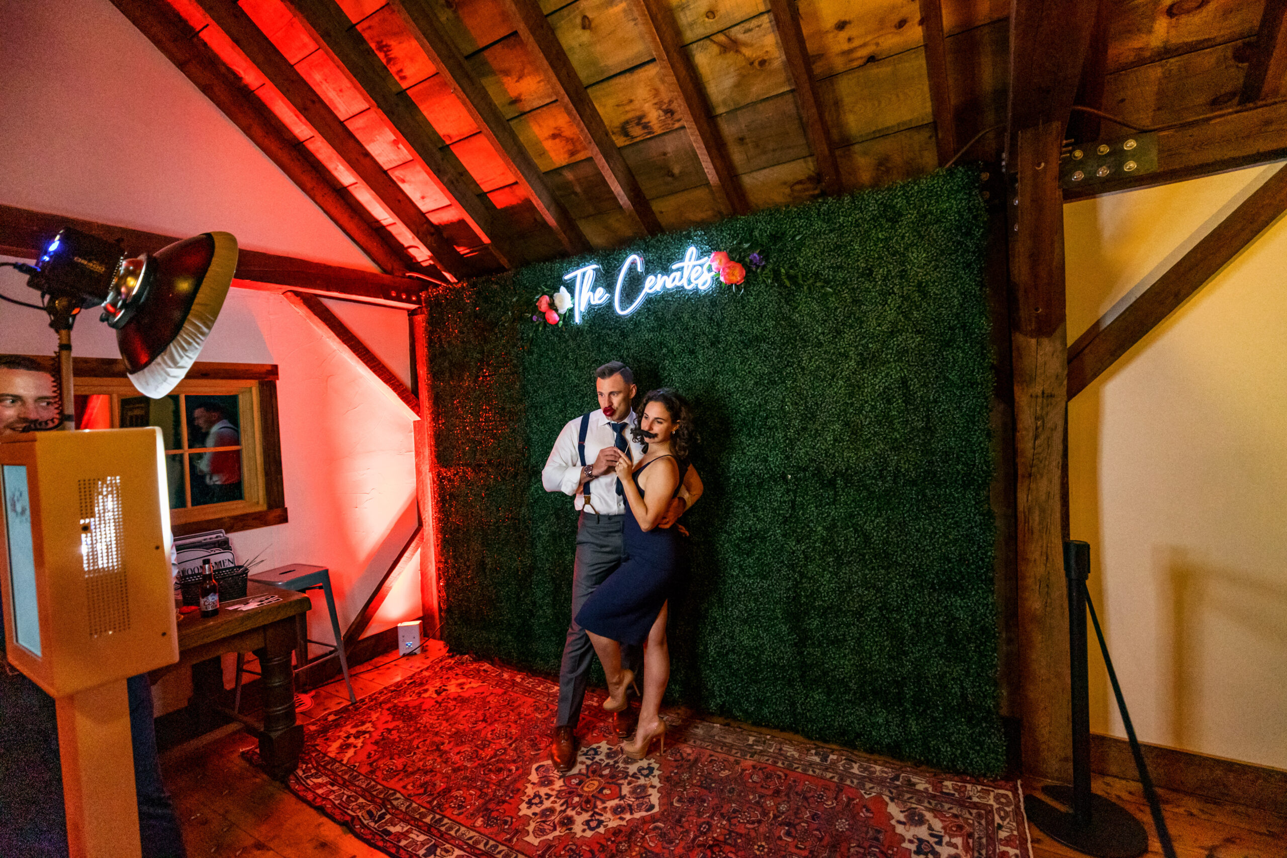 a couple poses with props in front of a wedding photo booth background with a custom neon sign hanging above